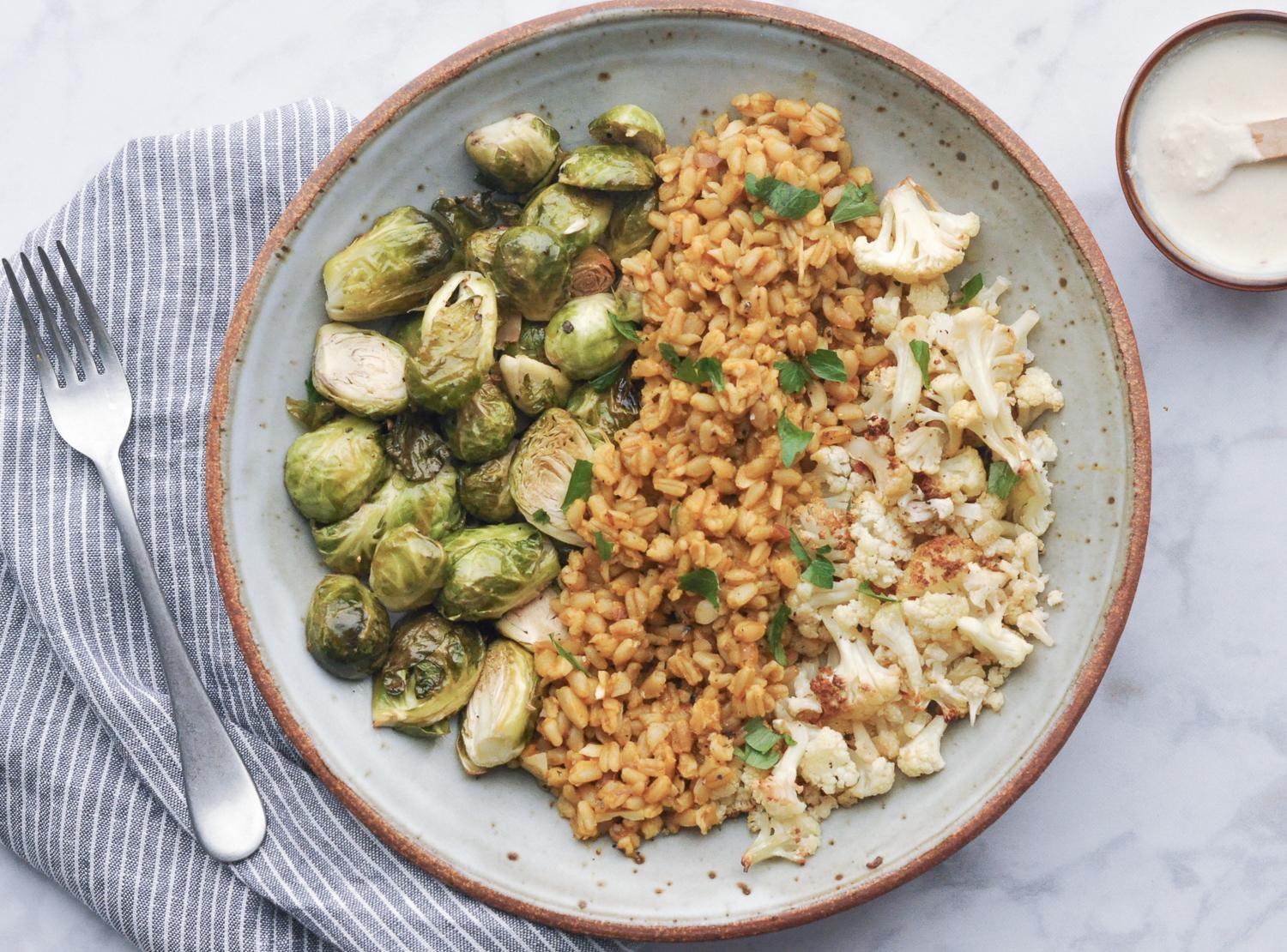 overhead shot of Freekeh Cream Cheese in a bowl with baguette slices and vegetables around it