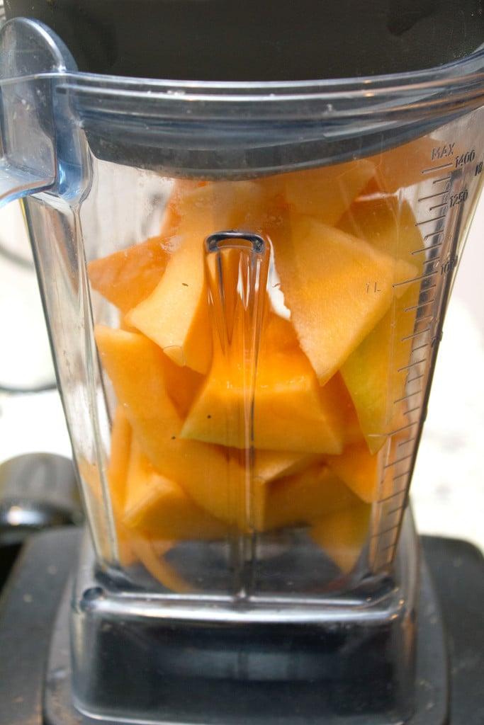 Overhead view of a person blending cantaloupe, mint, yogurt, and honey in a blender.