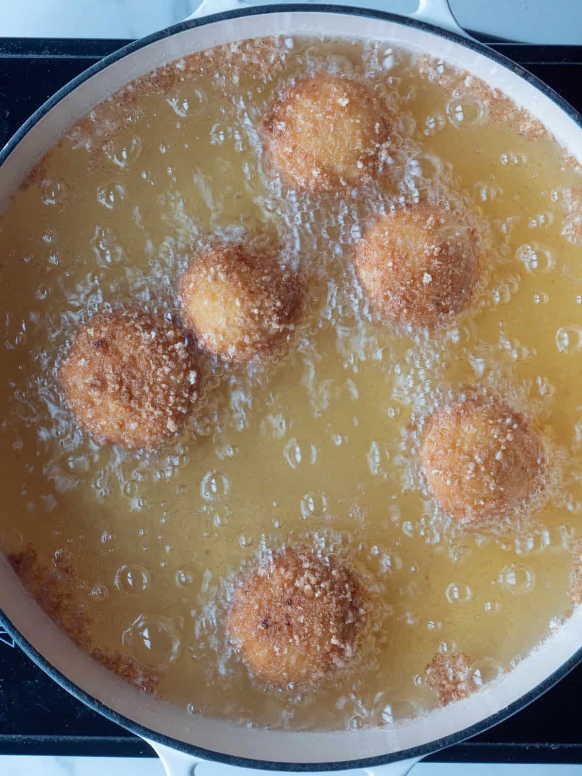 A close up shot of arancini being fried in oil
