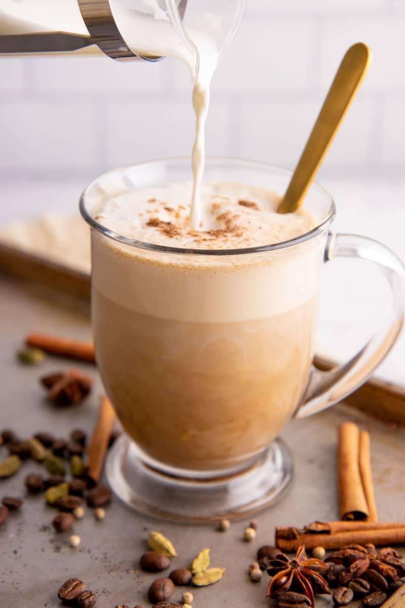 Maple cinnamon oat chai being poured into a glass mug in a cozy kitchen setting