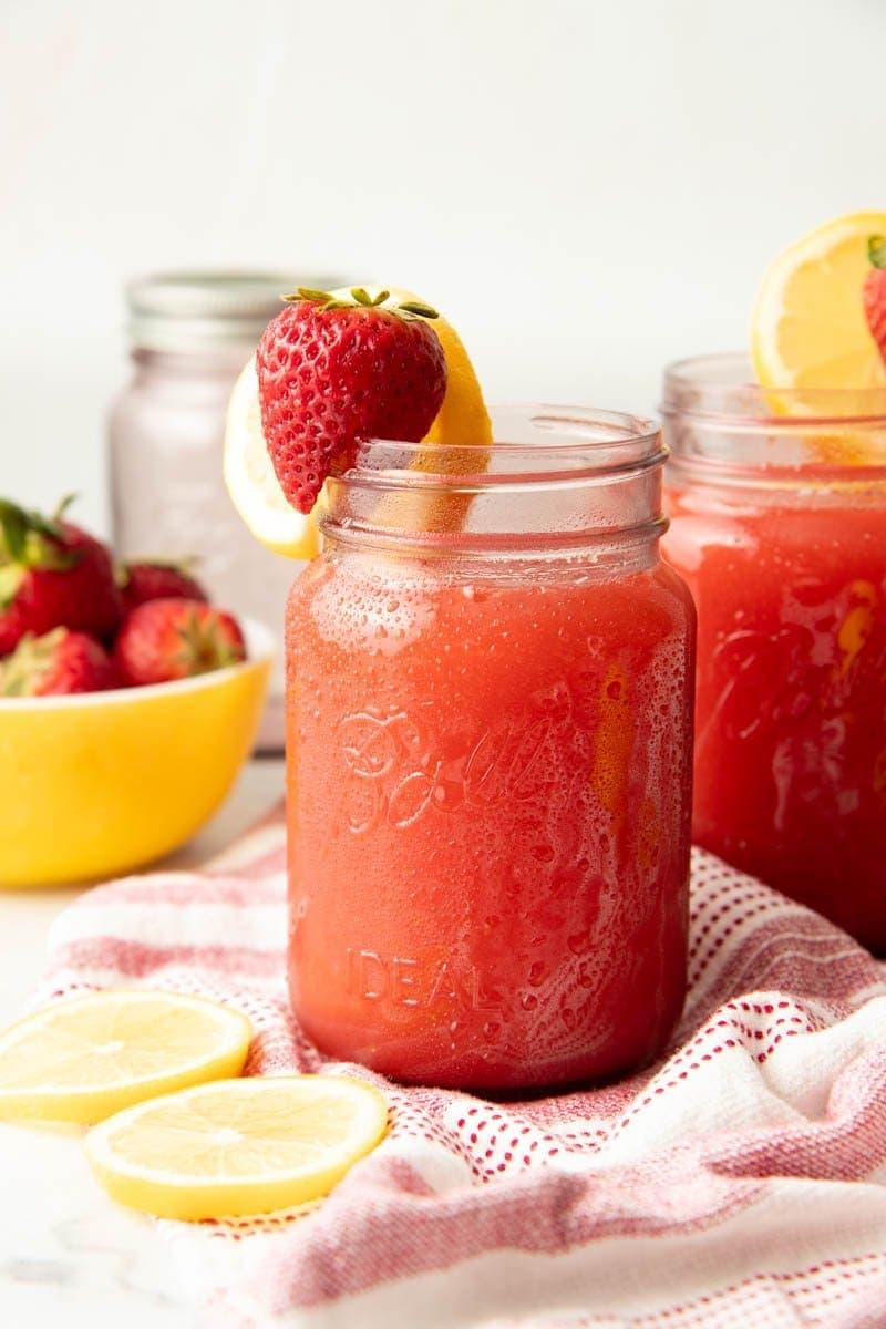 close up of a jar of strawberry lemonade preserves with fresh strawberries and lemons in the background