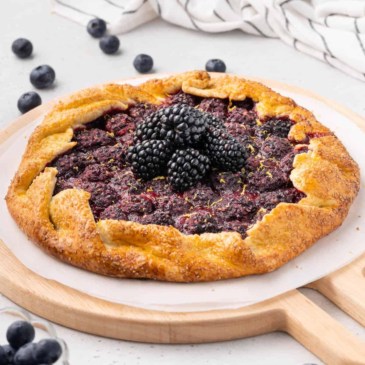 a whole blackberry Earl Grey tart on a rustic wooden table, surrounded by fresh blackberries and Earl Grey tea leaves