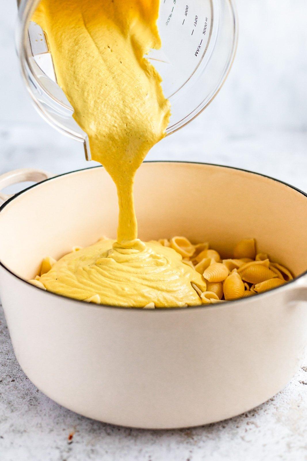 pouring vegan cheese sauce over pasta