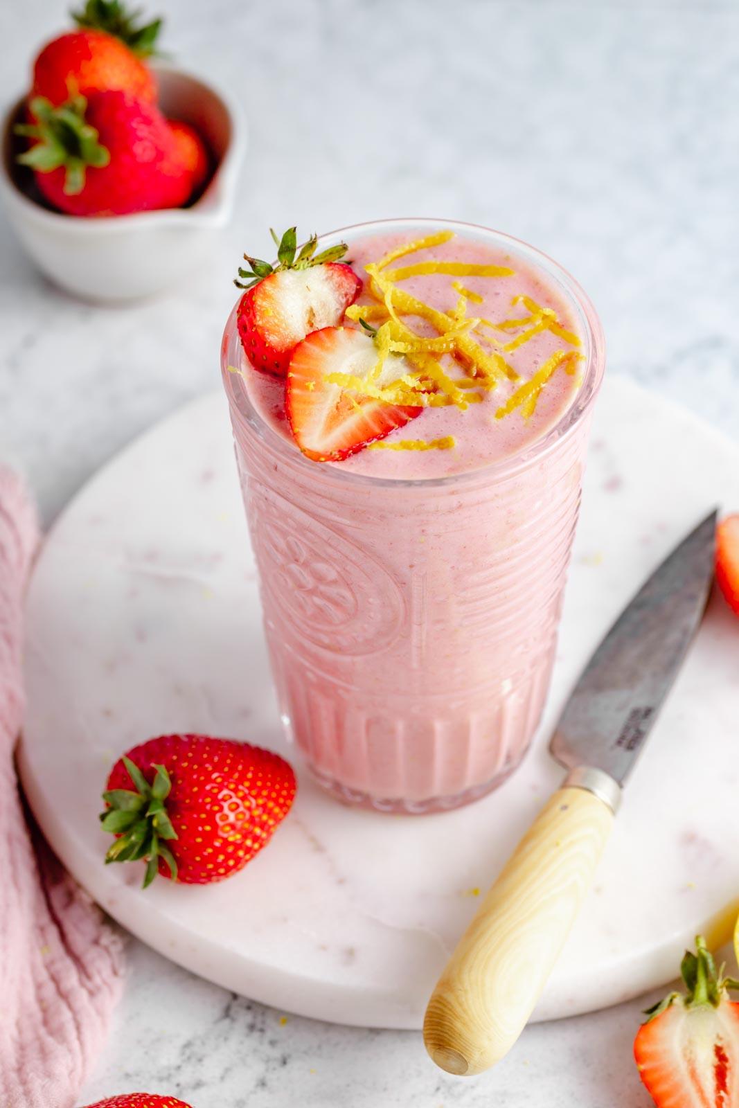 a refreshing strawberry lemonade dreamsicle smoothie in a glass with a straw, garnished with a strawberry and lemon slice