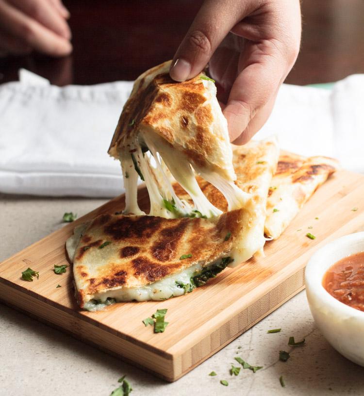 close-up shot of a spinach and ricotta quesadilla being cut open, revealing the melted cheese and spinach filling