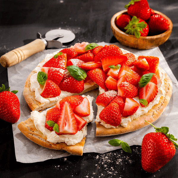 Ingredients for Strawberry Shortcake Pizza with Mascarpone arranged on a kitchen counter: strawberries, mascarpone cheese, pizza dough, butter, sugar, and vanilla extract