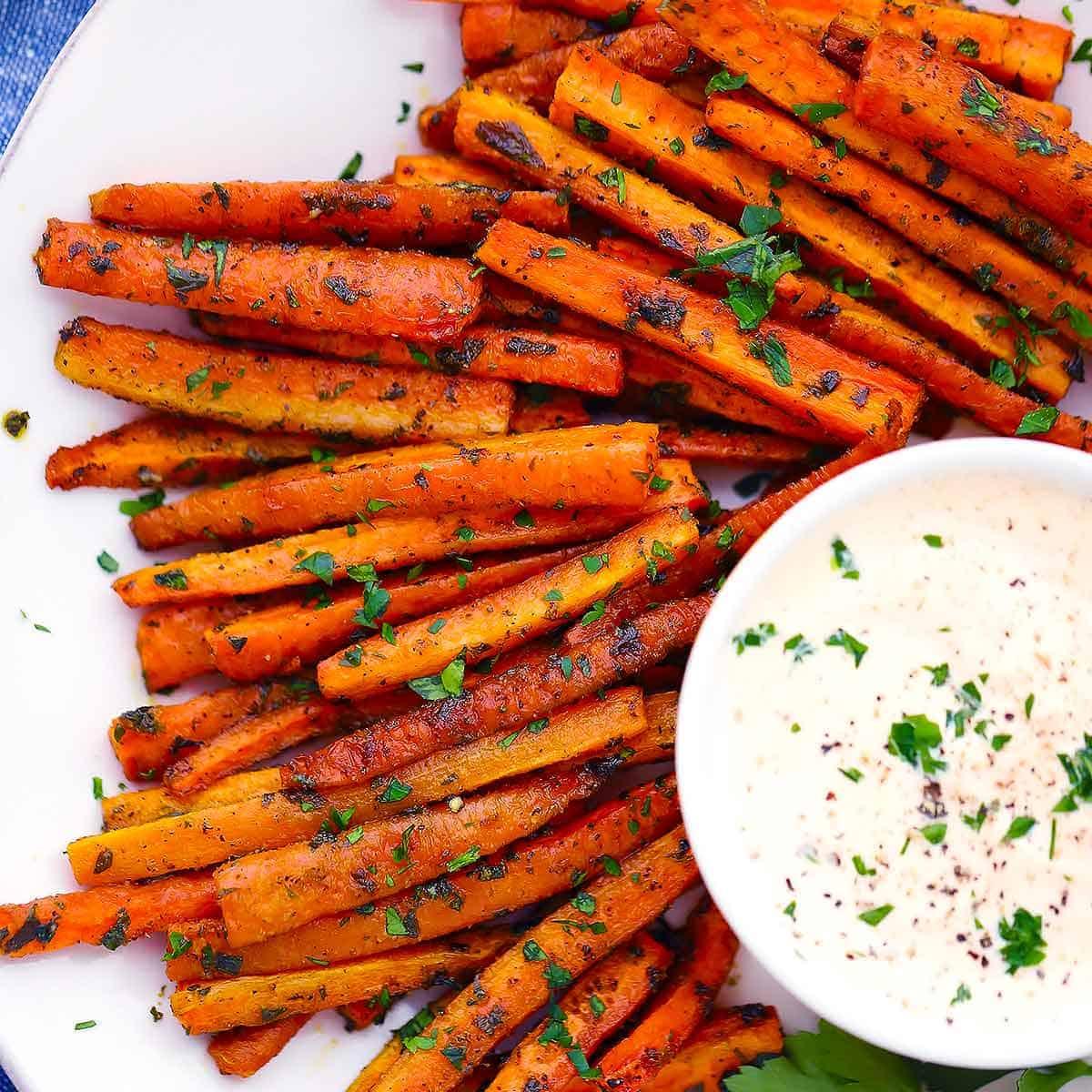 a person dipping a garlic herb roasted carrot fry into a dipping sauce