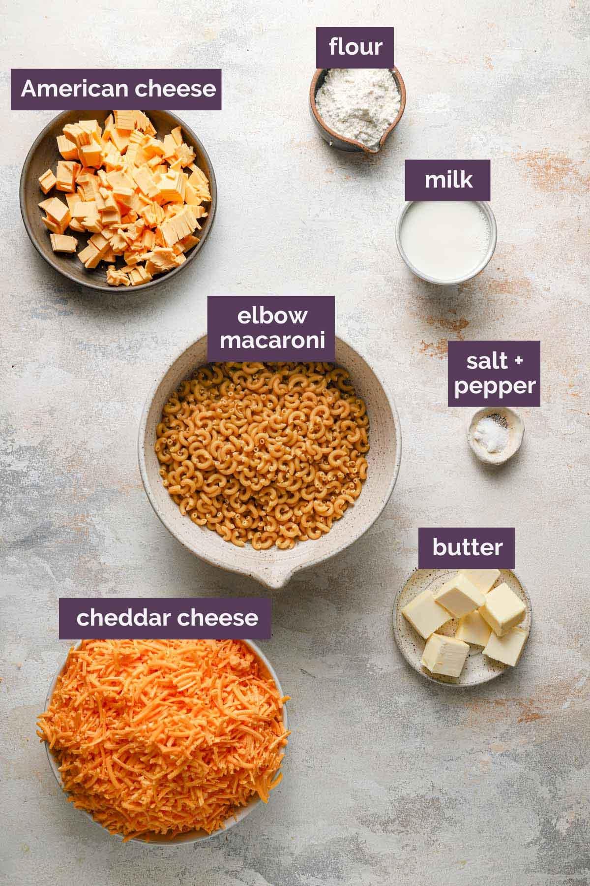 overhead shot of ingredients for spicy peanut mac and cheese laid out on a wooden table: macaroni, cheese, peanut butter, sriracha, milk, flour, butter