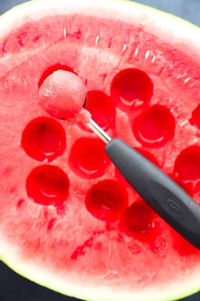 A hand tossing the watermelon fig prosciutto salad in a glass bowl