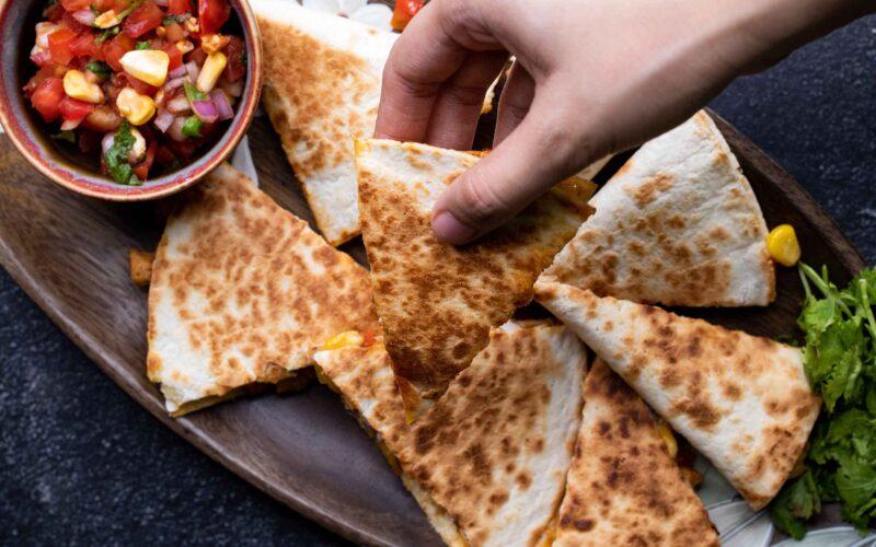 close-up of bbq chicken quesadilla being assembled with various toppings