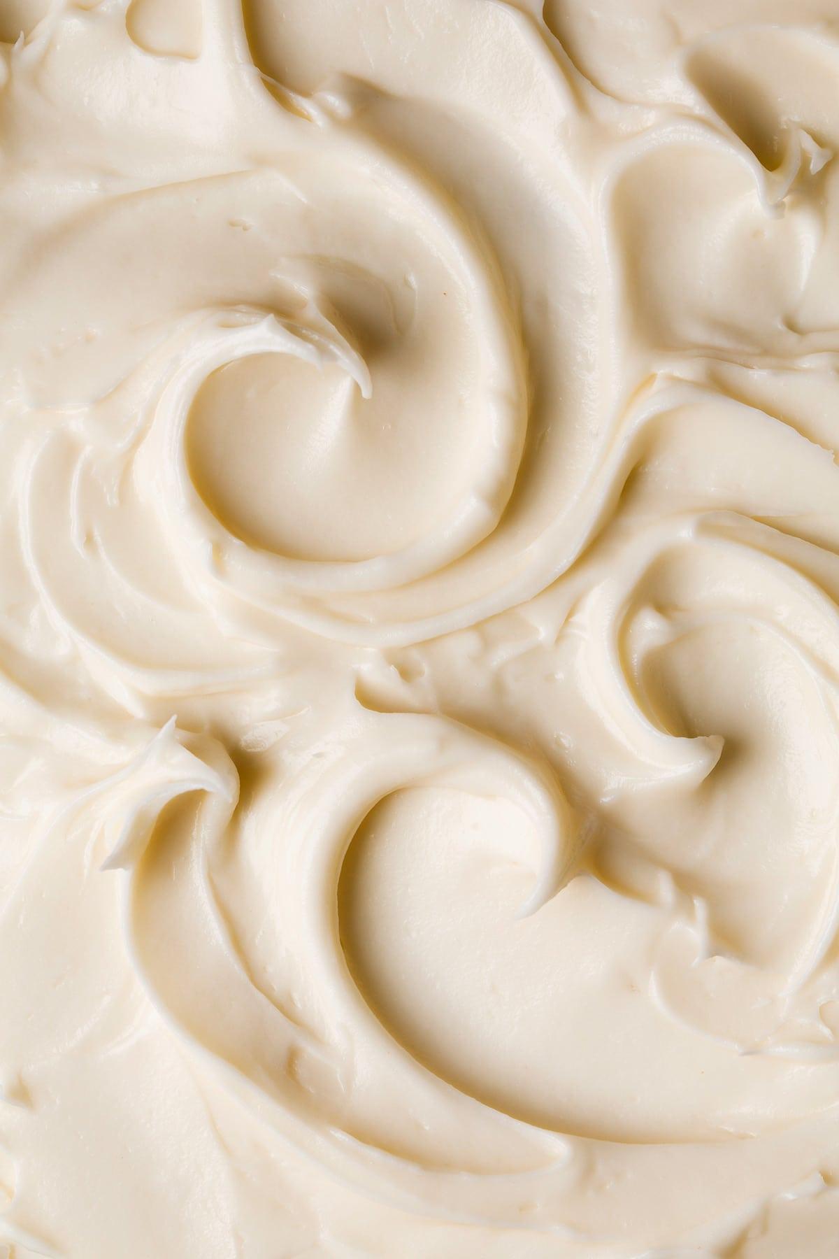 a close-up shot of the cream cheese frosting being swirled onto the cooled spice cake