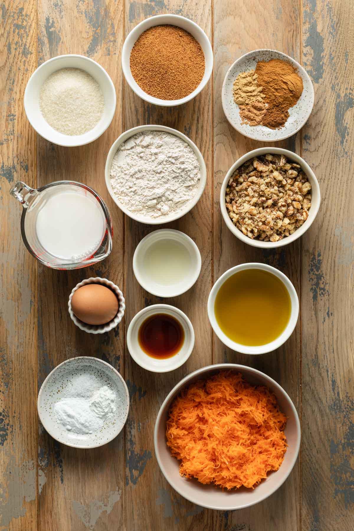 Ingredients for carrot cake, including carrots, flour, sugar, and spices, arranged on a wooden countertop