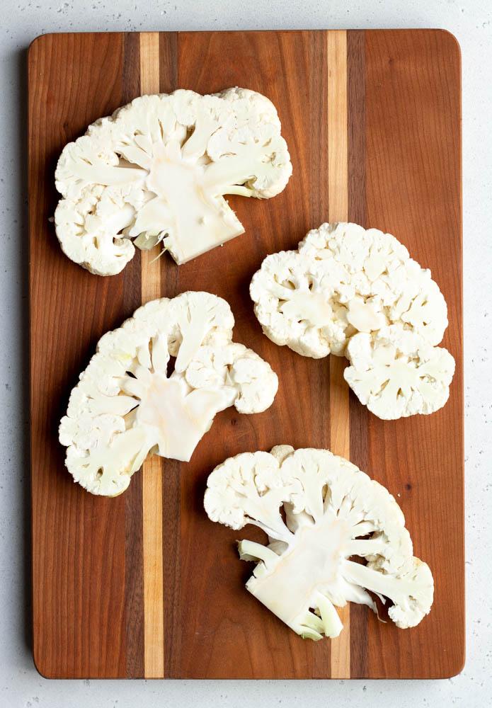 raw cauliflower being cut into steaks on a wooden cutting board