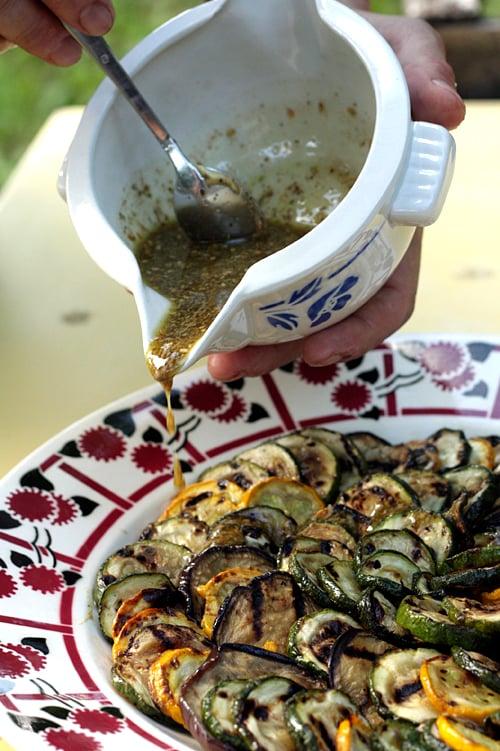close-up shot of the grilled vegetables being tossed with olive oil and seasonings in a mixing bowl