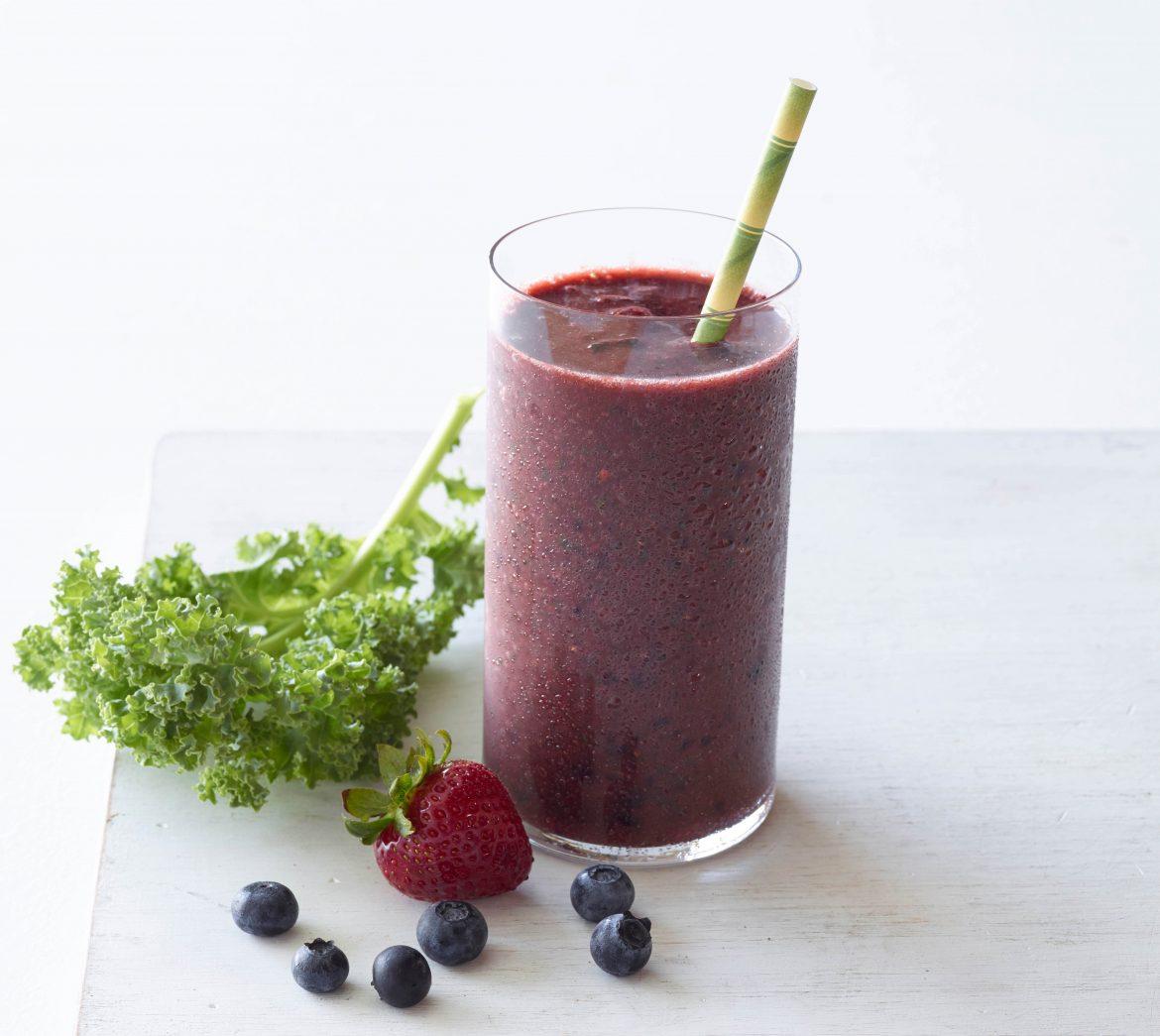 A glass of kombucha kale smoothie with a person preparing it in the background