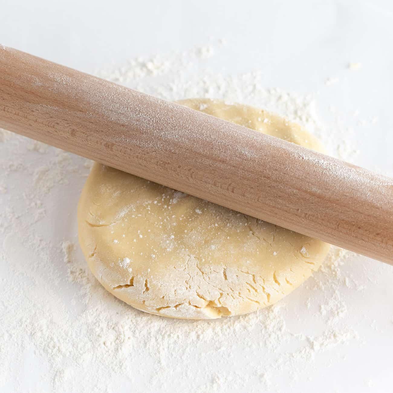 Homemade sugar cookie dough being rolled out on a floured surface, hands visible