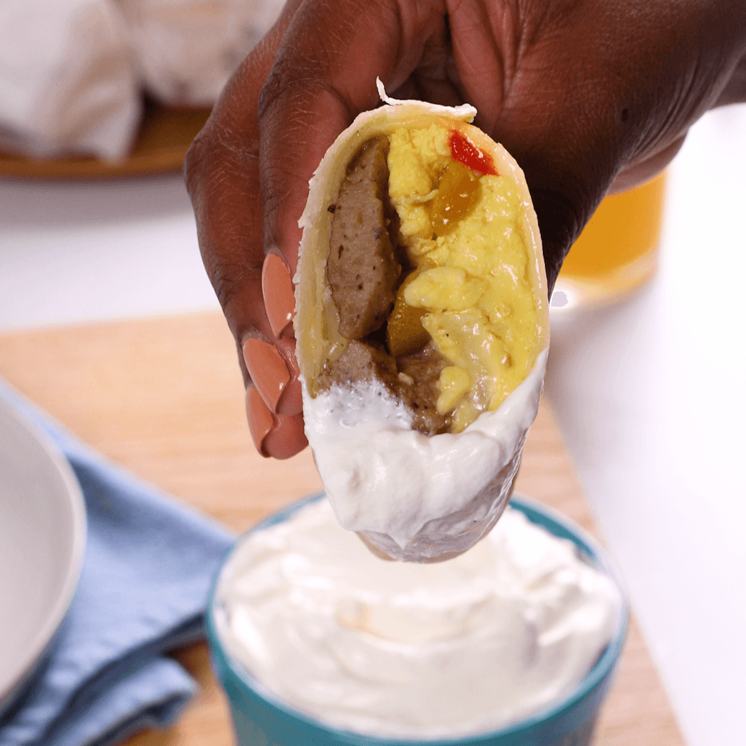 hand holding a half-eaten crispy breakfast burrito melt, showing gooey cheese and fillings