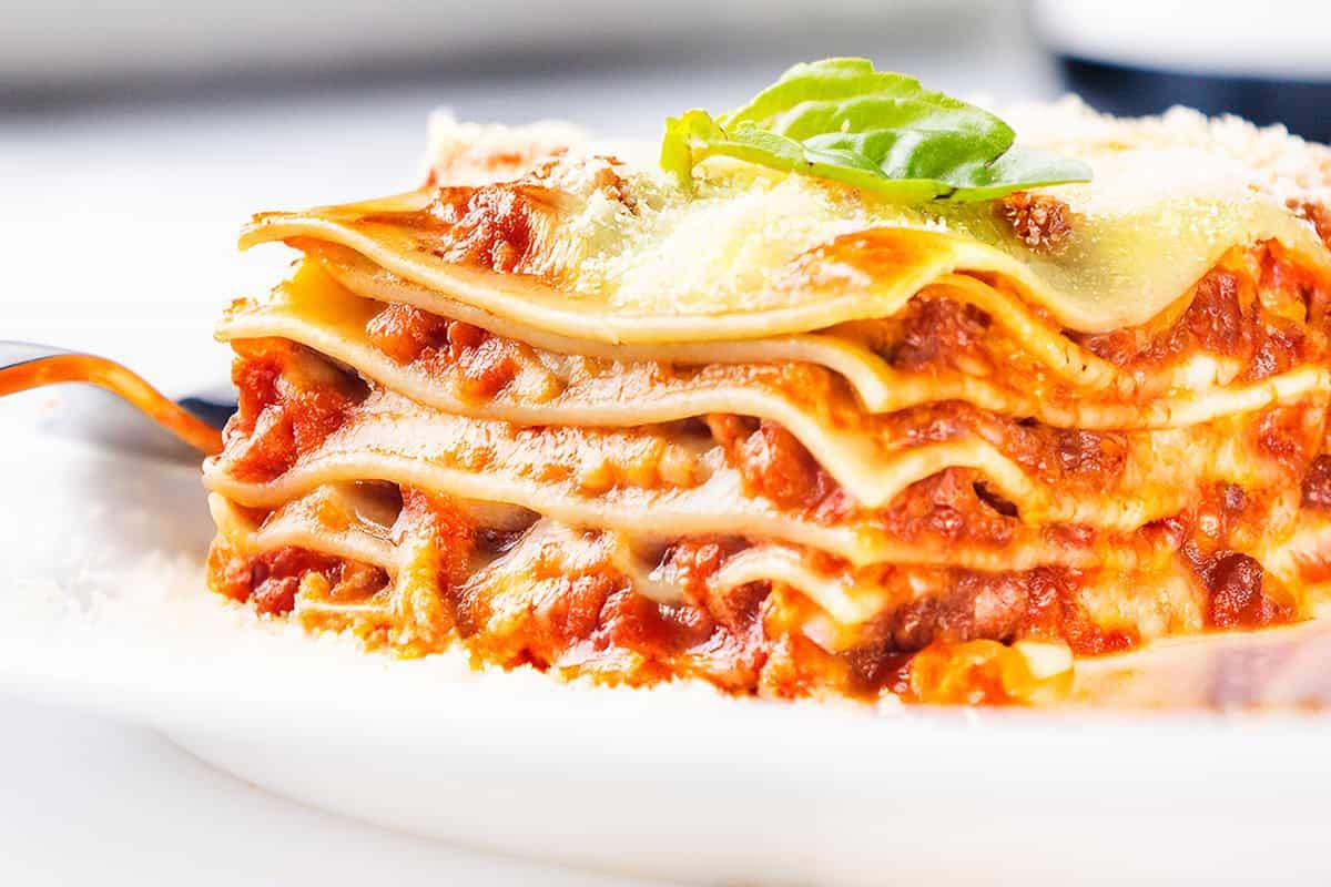 Close-up of a slice of breakfast lasagna showing the layers of noodles, cheese, and sausage gravy