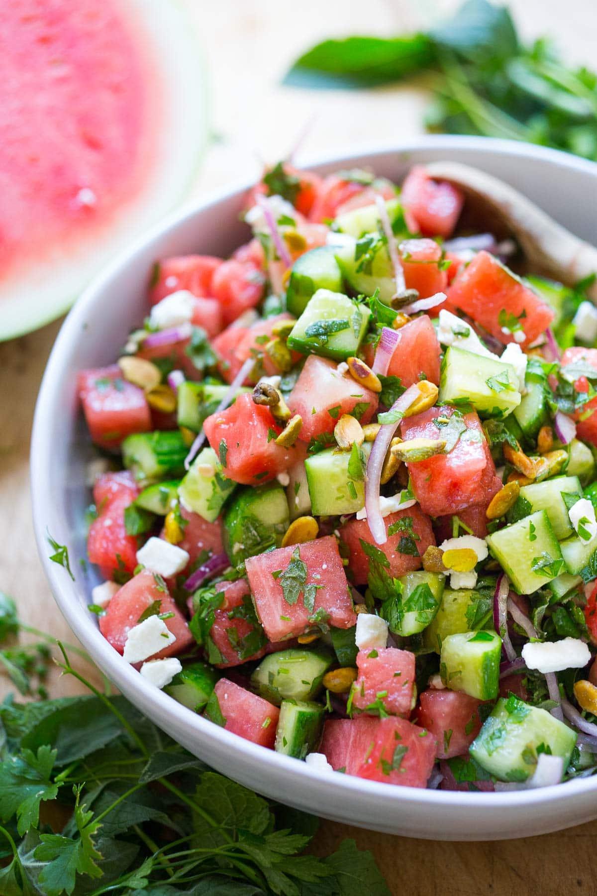 a person happily enjoying a bowl of watermelon cucumber pasta salad outdoors