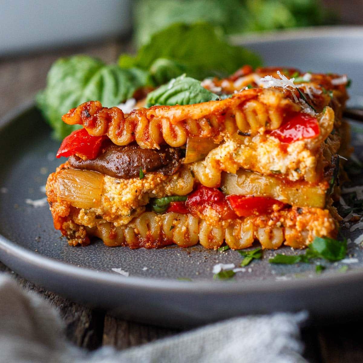 layers of lasagna being assembled in a baking dish, showing pasta, roasted vegetables, goat cheese, and sauce