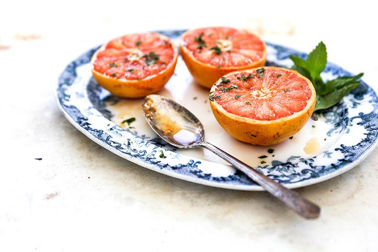 plate with two grilled grapefruit halves garnished with mint, served on a wooden table