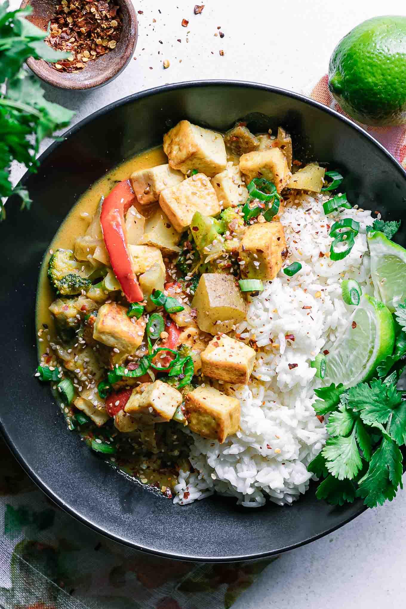 A bowl of yellow curry tofu stir-fry with bok choy served over rice, garnished with sesame seeds and cilantro
