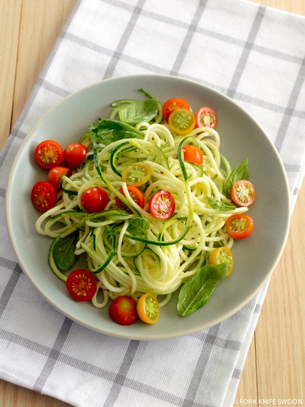 close up of fresh zucchini noodles with cherry tomatoes and basil