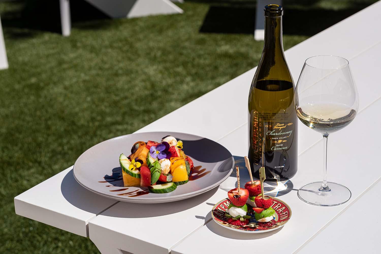 A person enjoying a Caprese salad with a glass of white wine in a sunlit setting
