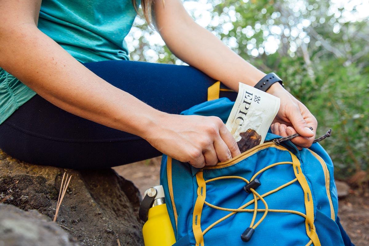 a person hiking on a mountain trail reaching into their backpack for a trail mix bar