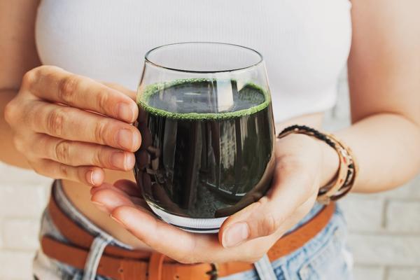 Person holding a glass of spirulina mint cold brew outdoors in natural light