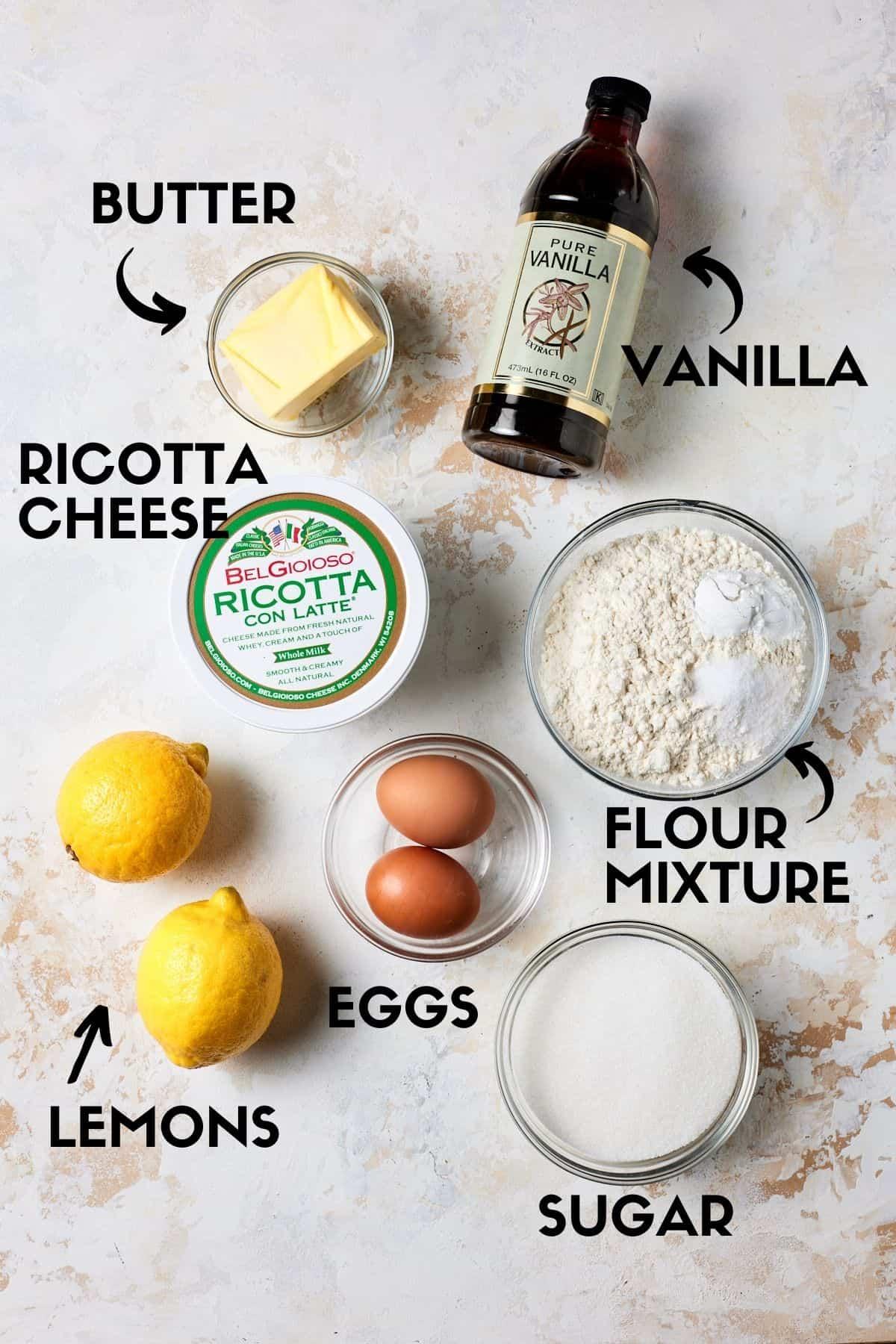 ingredients for lemon ricotta cake, including lemons, ricotta cheese, flour, and eggs