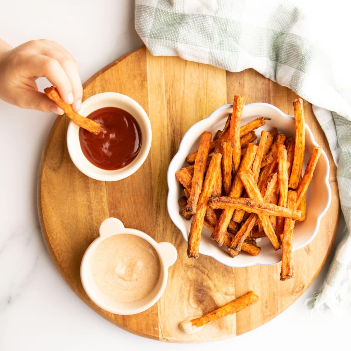 A person tossing carrot fries with date syrup glaze in a bowl