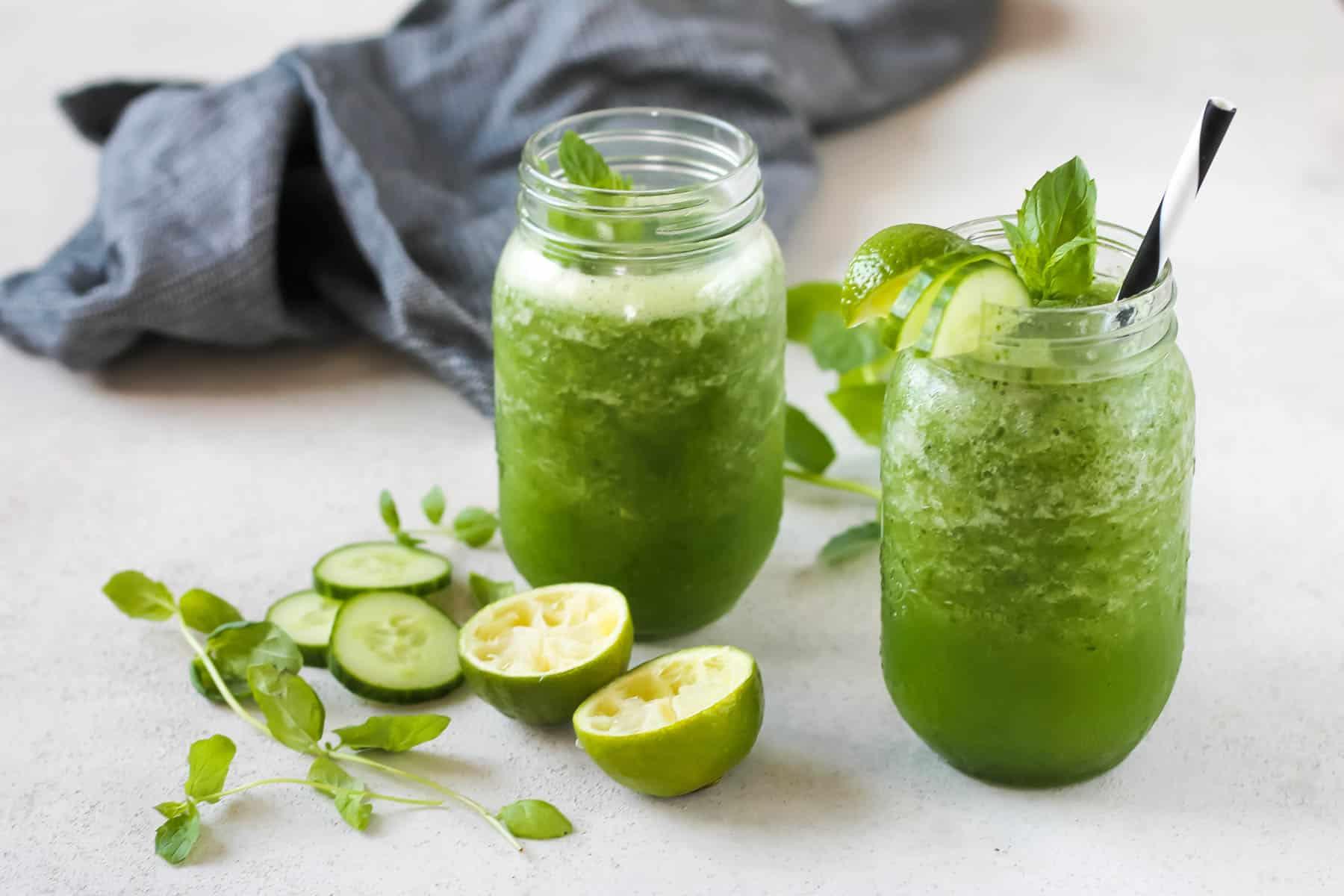 a blender in action, blending cucumbers, mint, lime juice, and water, with a blurred background showing a bright kitchen setting