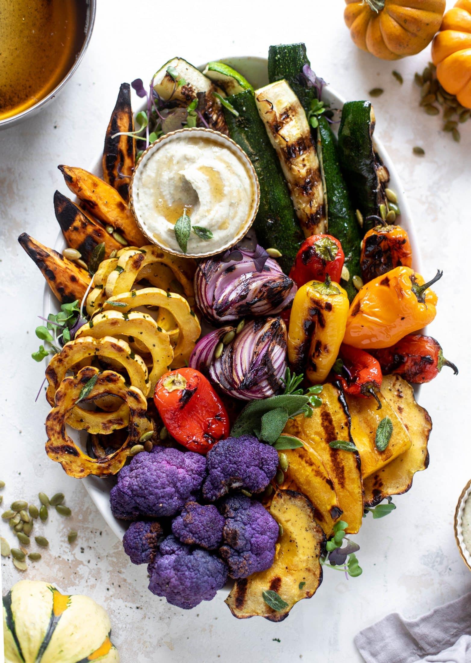 Overhead shot of a colorful platter of sage-butter vegetables, surrounded by various grilled meats and sides