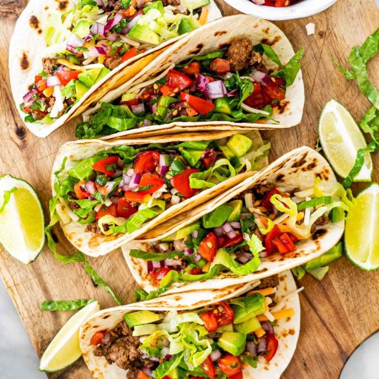 Overhead shot of hands assembling Zinfandel Reduction Ground Beef Tacos with various toppings