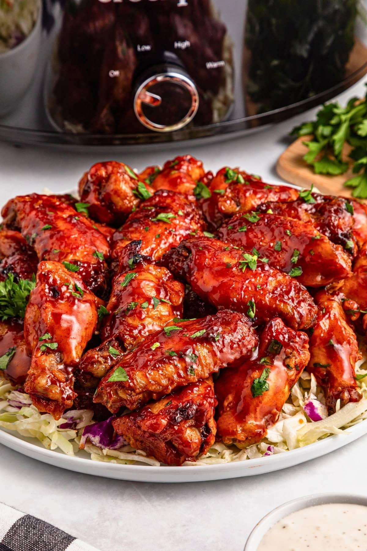 slow cooker filled with spicy peach BBQ chicken wings, garnished with fresh herbs