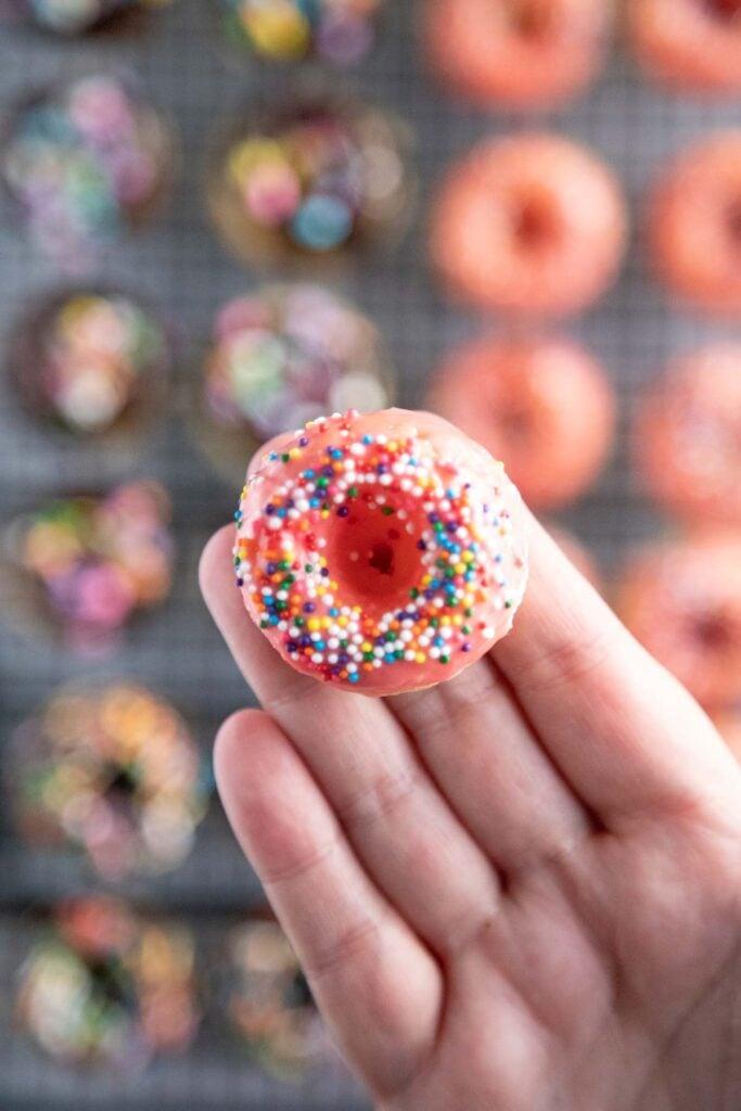 A close-up shot of a hand dipping a mini donut into red glaze.