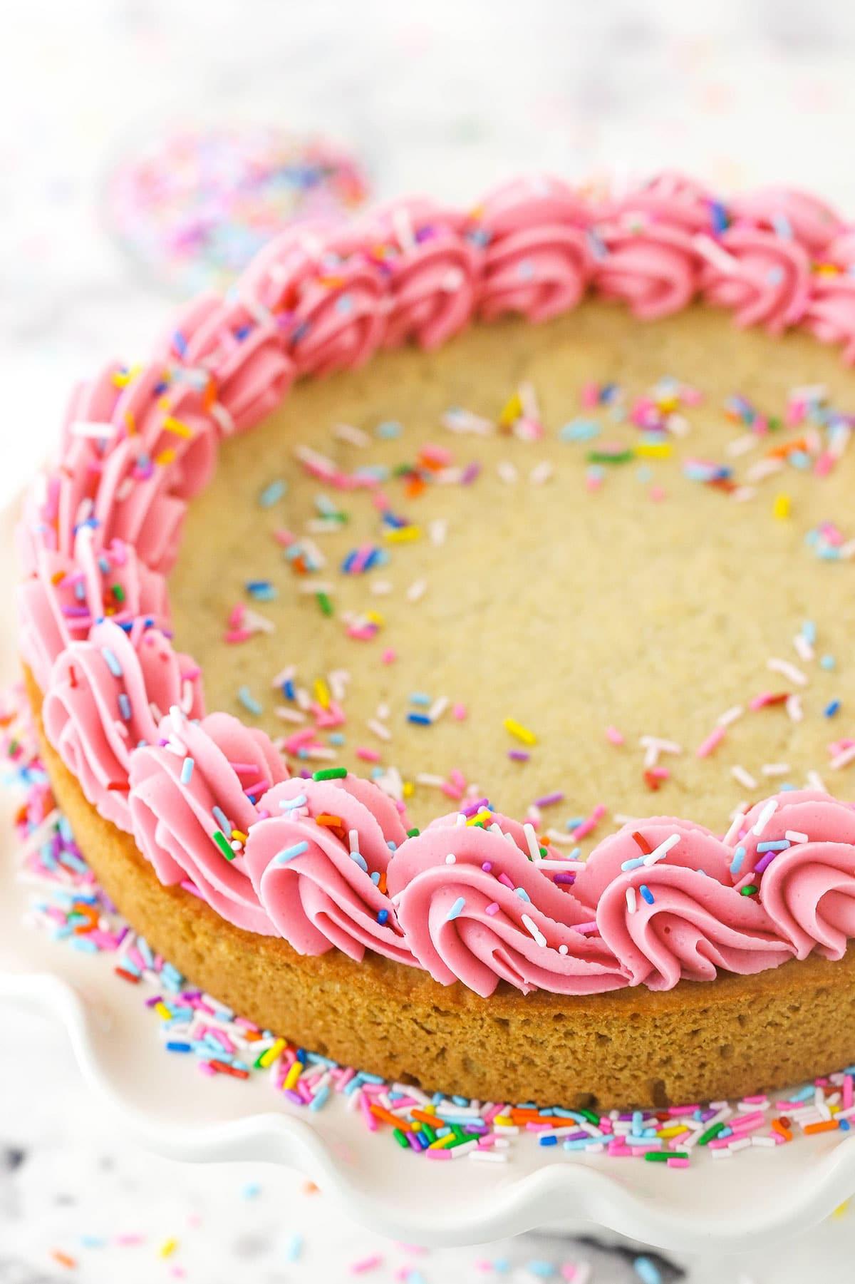 overhead shot of a large, round cookie cake decorated with frosting and sprinkles