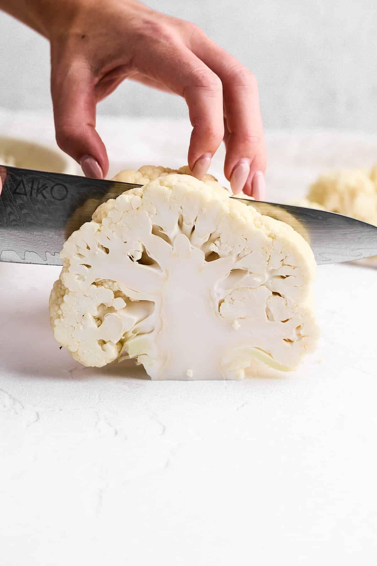 raw cauliflower head being sliced into steaks