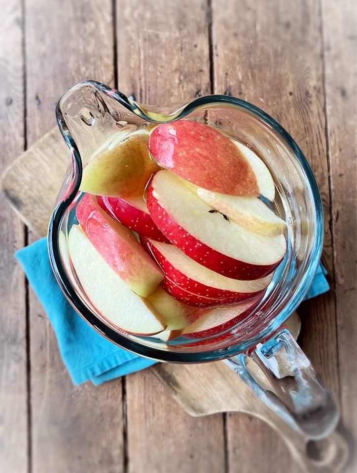 overhead shot of a bowl of blue colored water with apple slices soaking inside