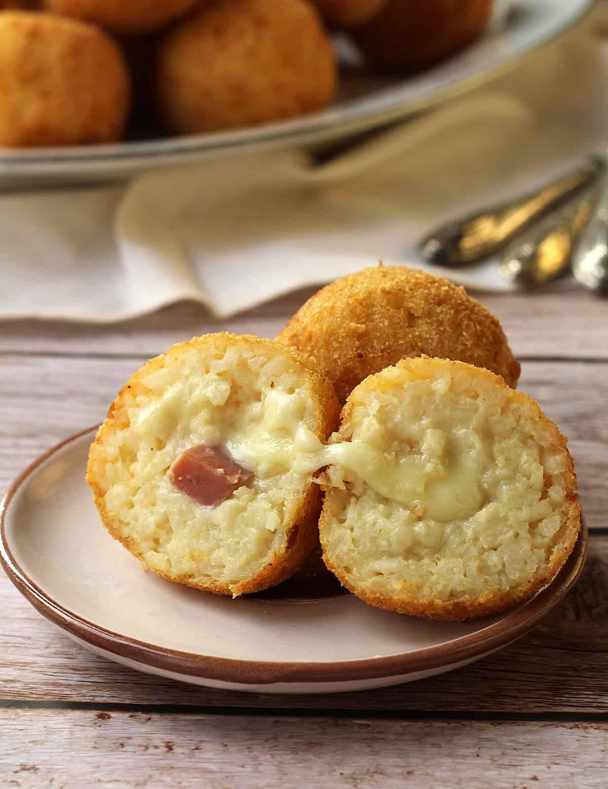A person cutting an arancini in half to reveal the cheesy filling