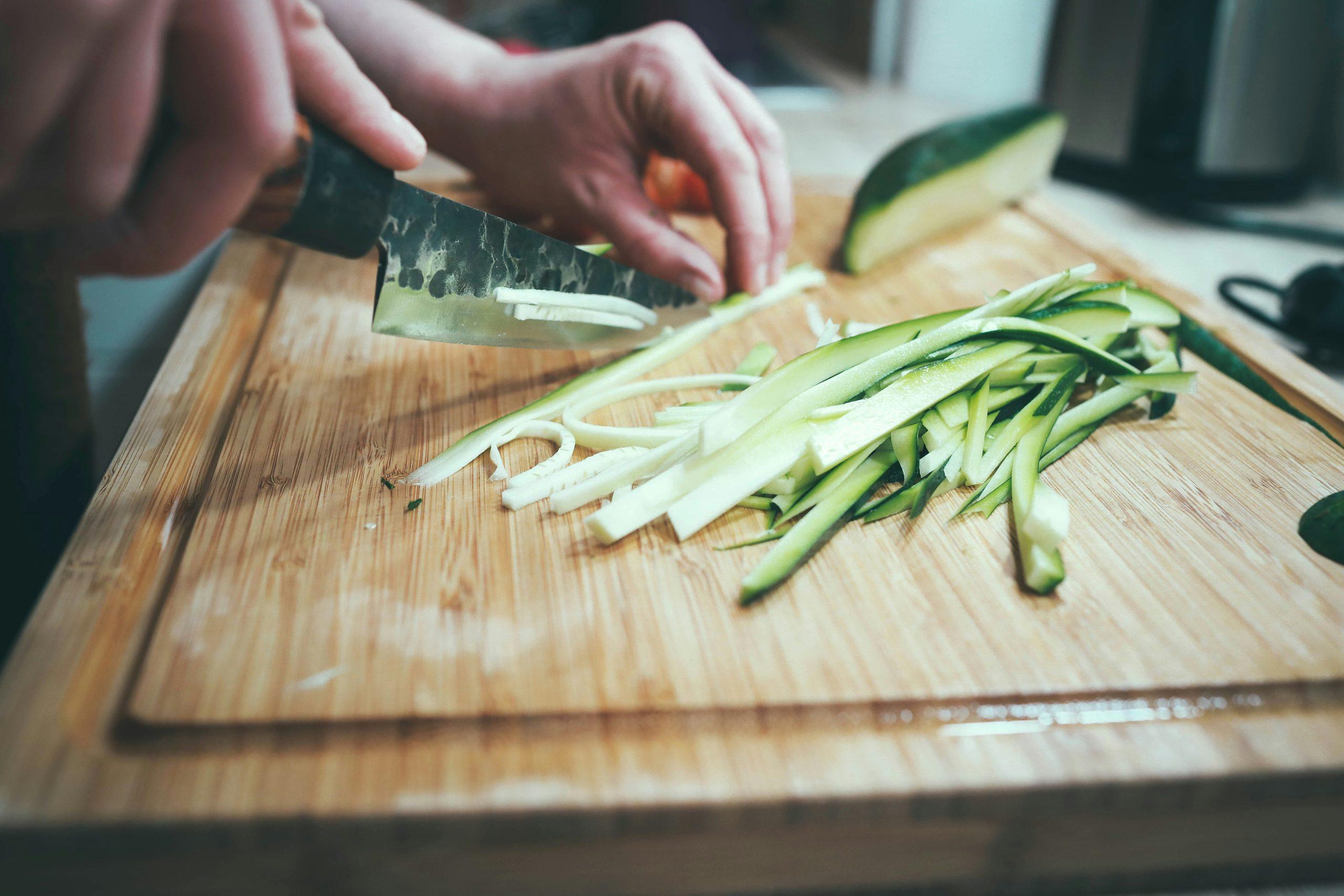 raw zucchini and bok choy being prepped on a wooden cutting board.