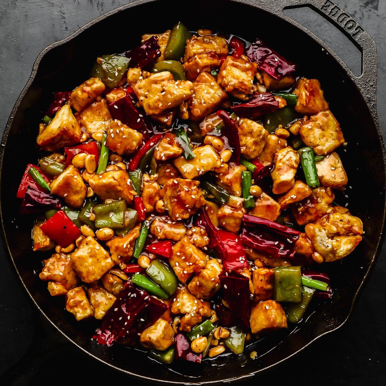 A plate of Kung Pao Tofu next to a bowl of peanuts and dried chilies