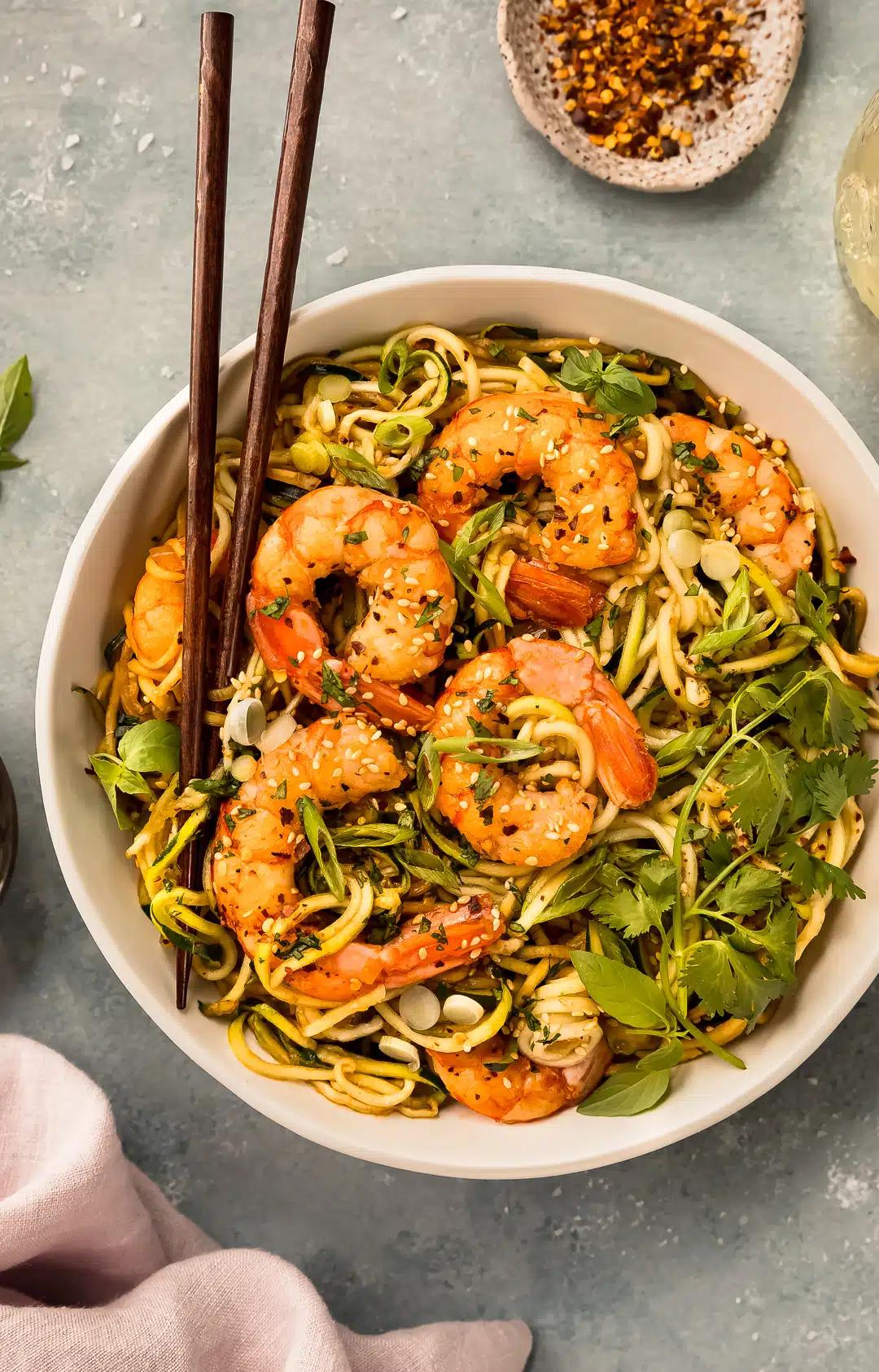 zucchini noodles and shirataki noodles with shrimp, peanuts, and lime wedges in a bowl
