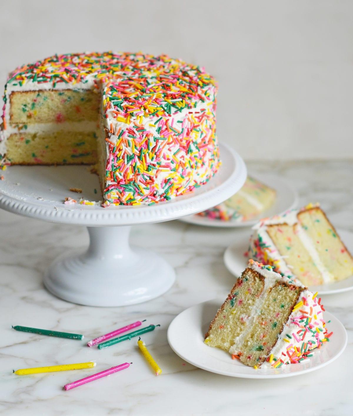 hands decorating a vanilla birthday cake with shimmering sprinkles