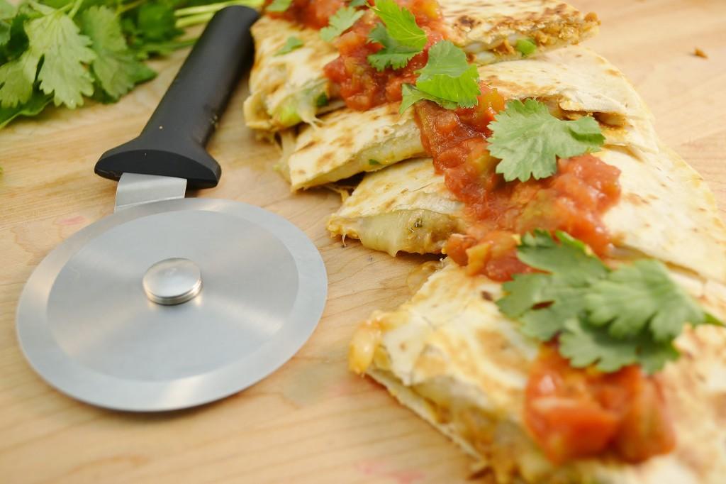 a hand cutting a bbq chicken quesadilla with a pizza cutter