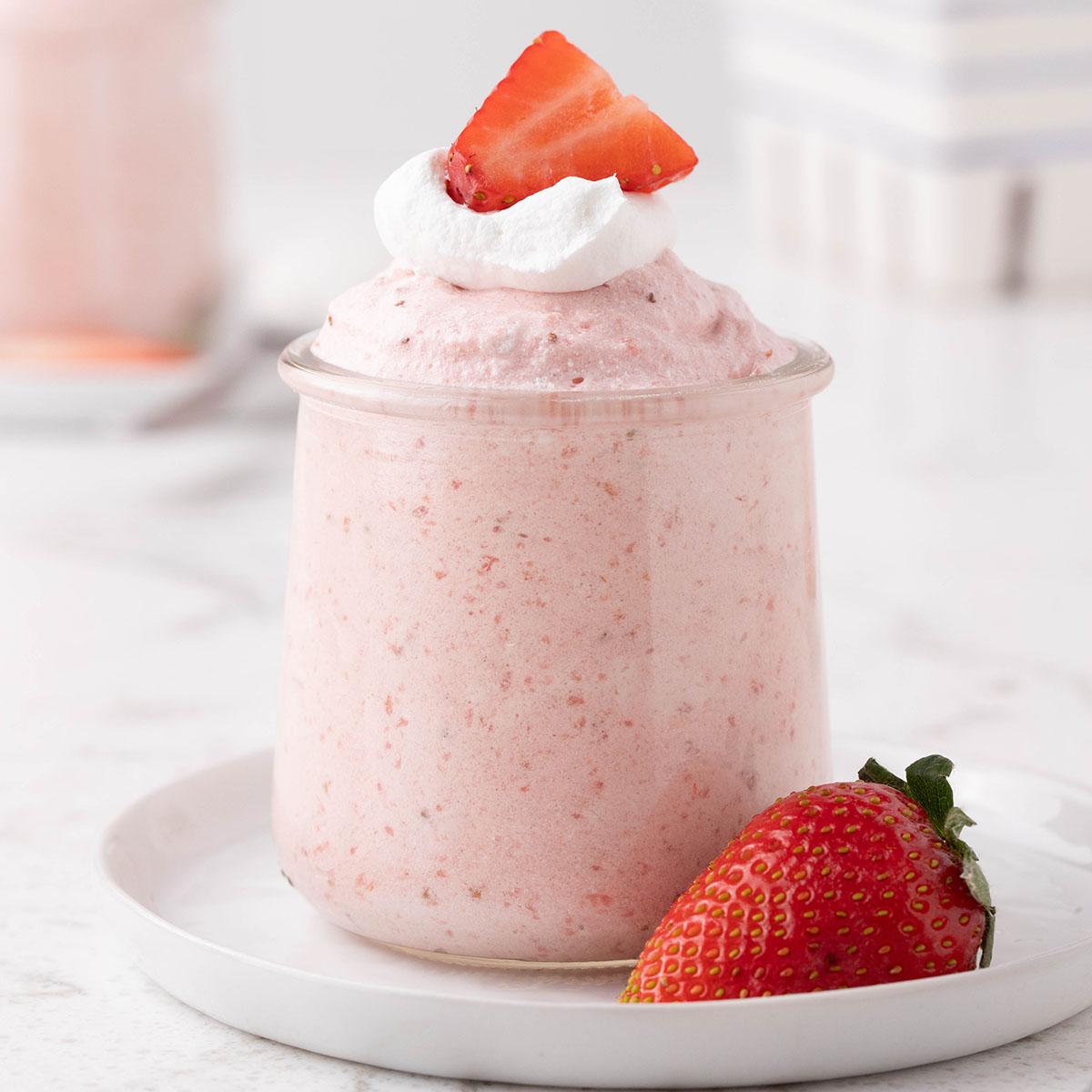 ingredients for strawberry mousse ice cream floats arranged on a kitchen counter: fresh strawberries, strawberry ice cream, whipped cream, sparkling water, and a bottle of strawberry liqueur