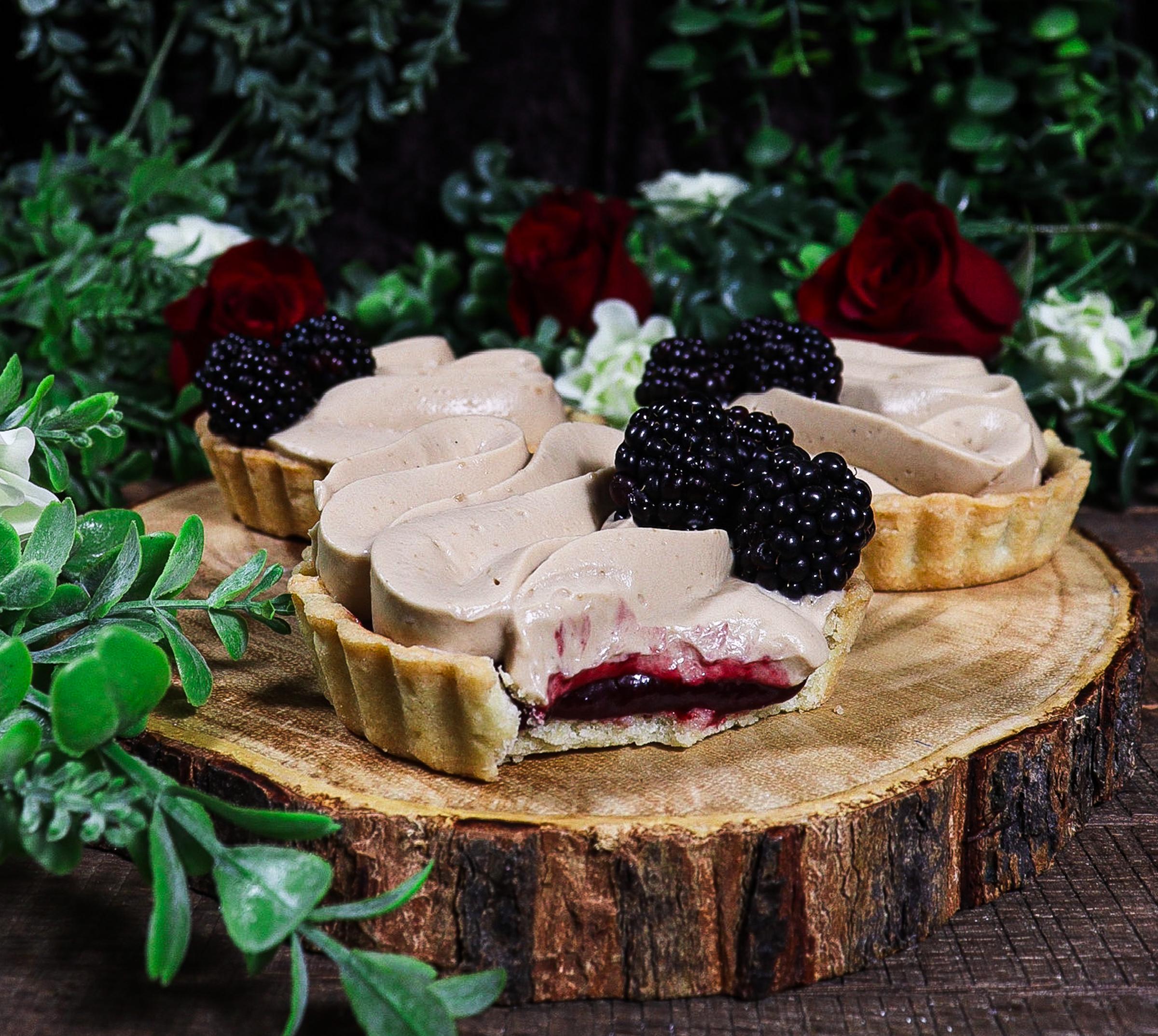 a slice of blackberry Earl Grey tart being lifted from the tart, showing the layers of crust, blackberry filling, and Earl Grey cream