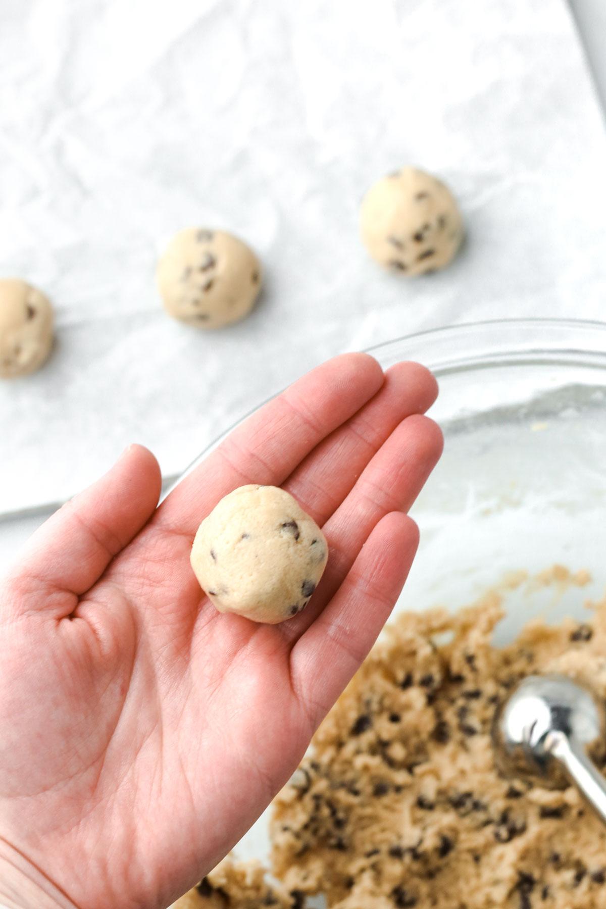 hands rolling cookie dough into balls, with various mix-ins (chocolate chips, marshmallows, almonds) scattered around