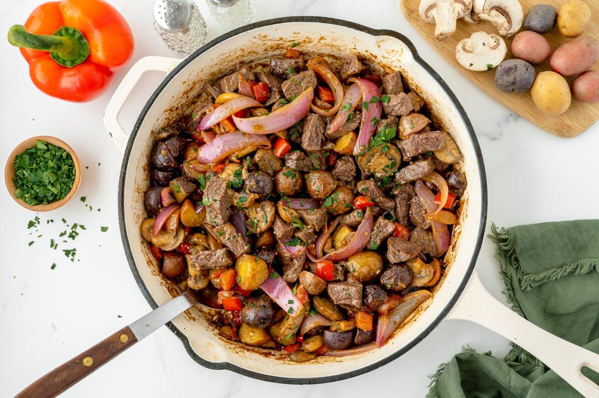 Overhead shot of a cast iron skillet with sautéed steak, onions, and bell peppers